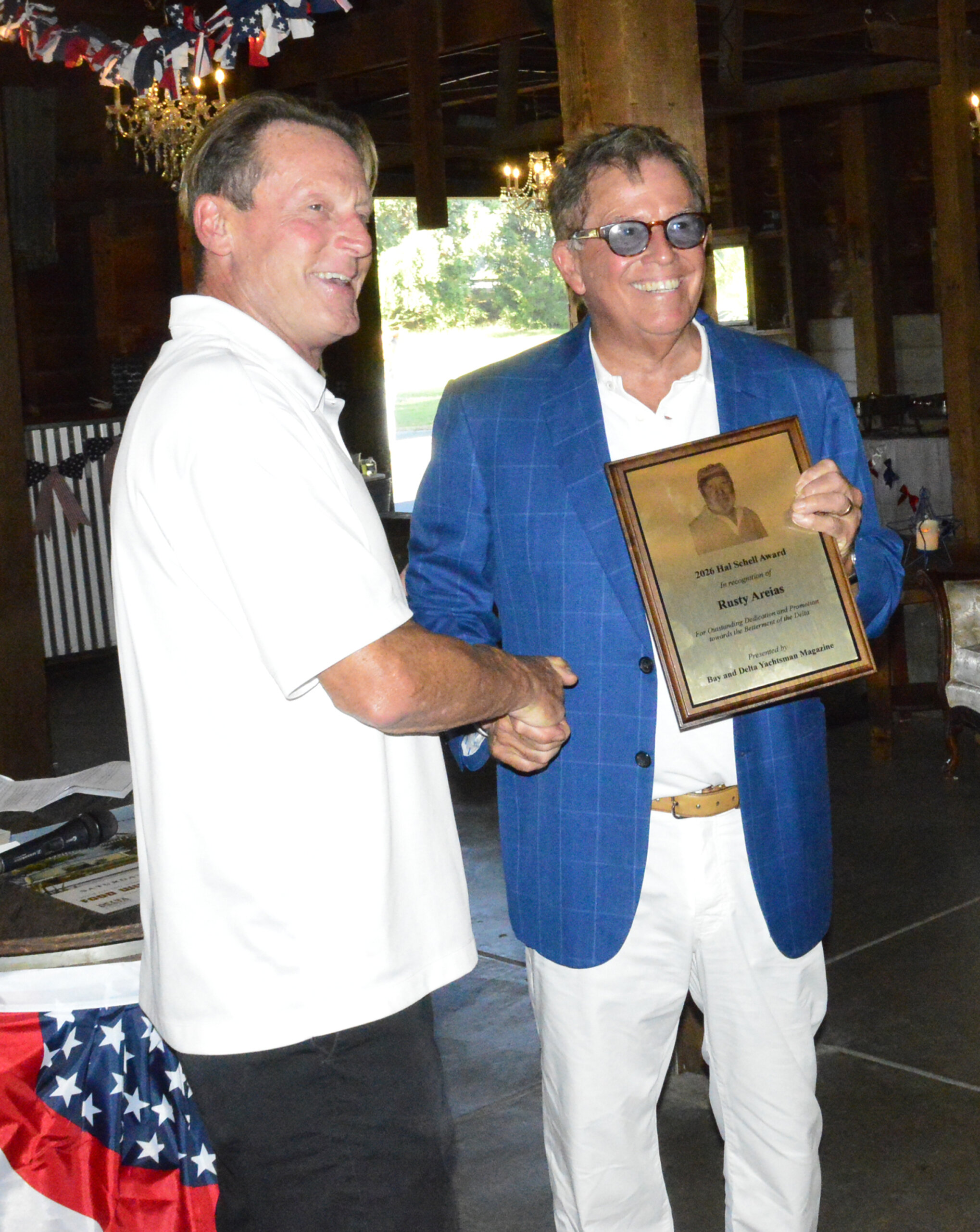 Rusty Areias in a blue blazer shakes hands while holding the 2026 Hal Schell Award plaque.