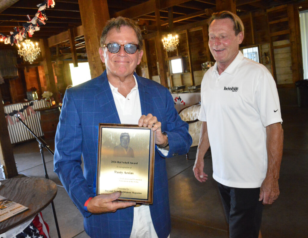Rusty Areias holds the 2026 Hal Schell Award plaque beside an event presenter.