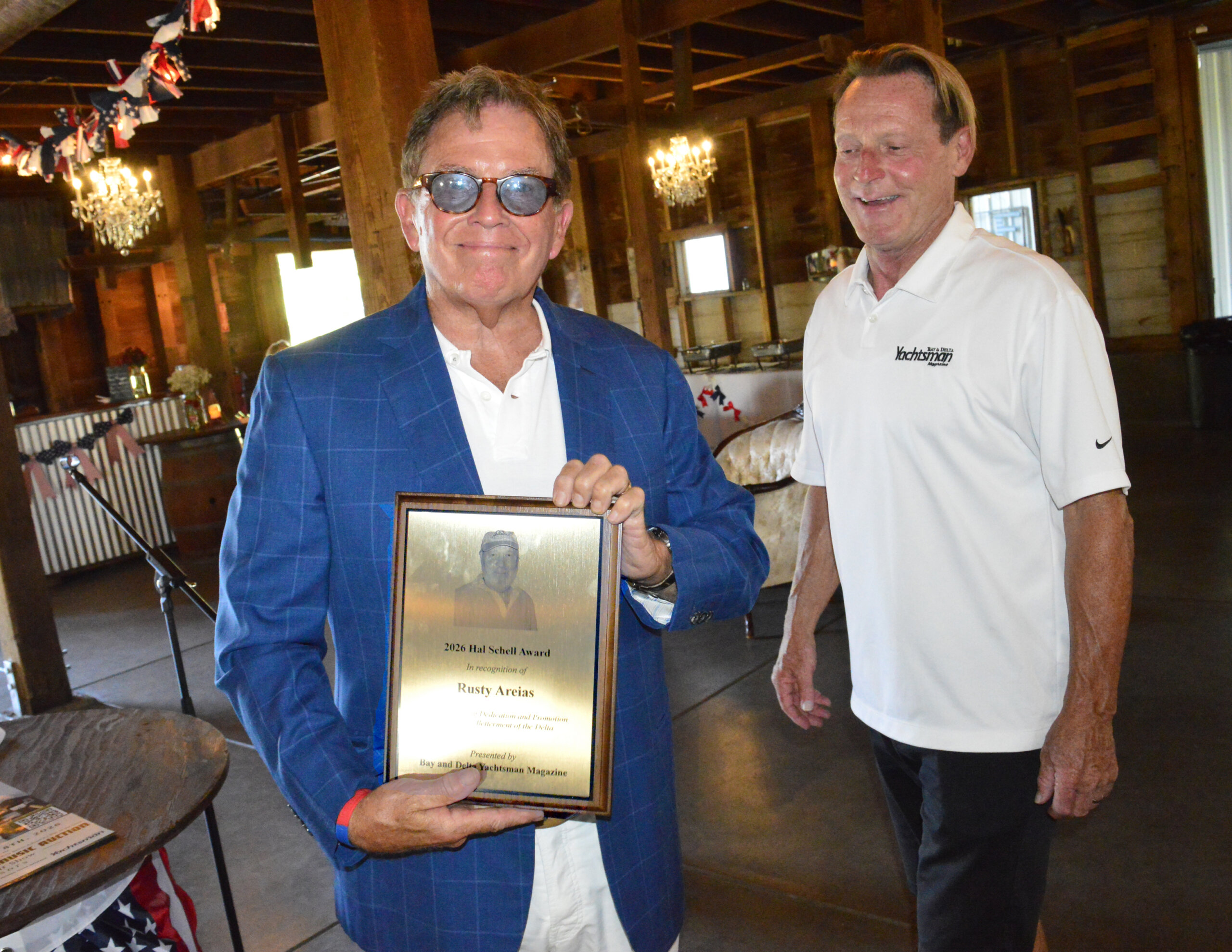 Rusty Areias holds the 2026 Hal Schell Award plaque beside an event presenter.